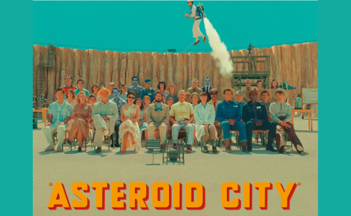 people seated in front of fence as man takes off like a rocket behind them Asteroid City